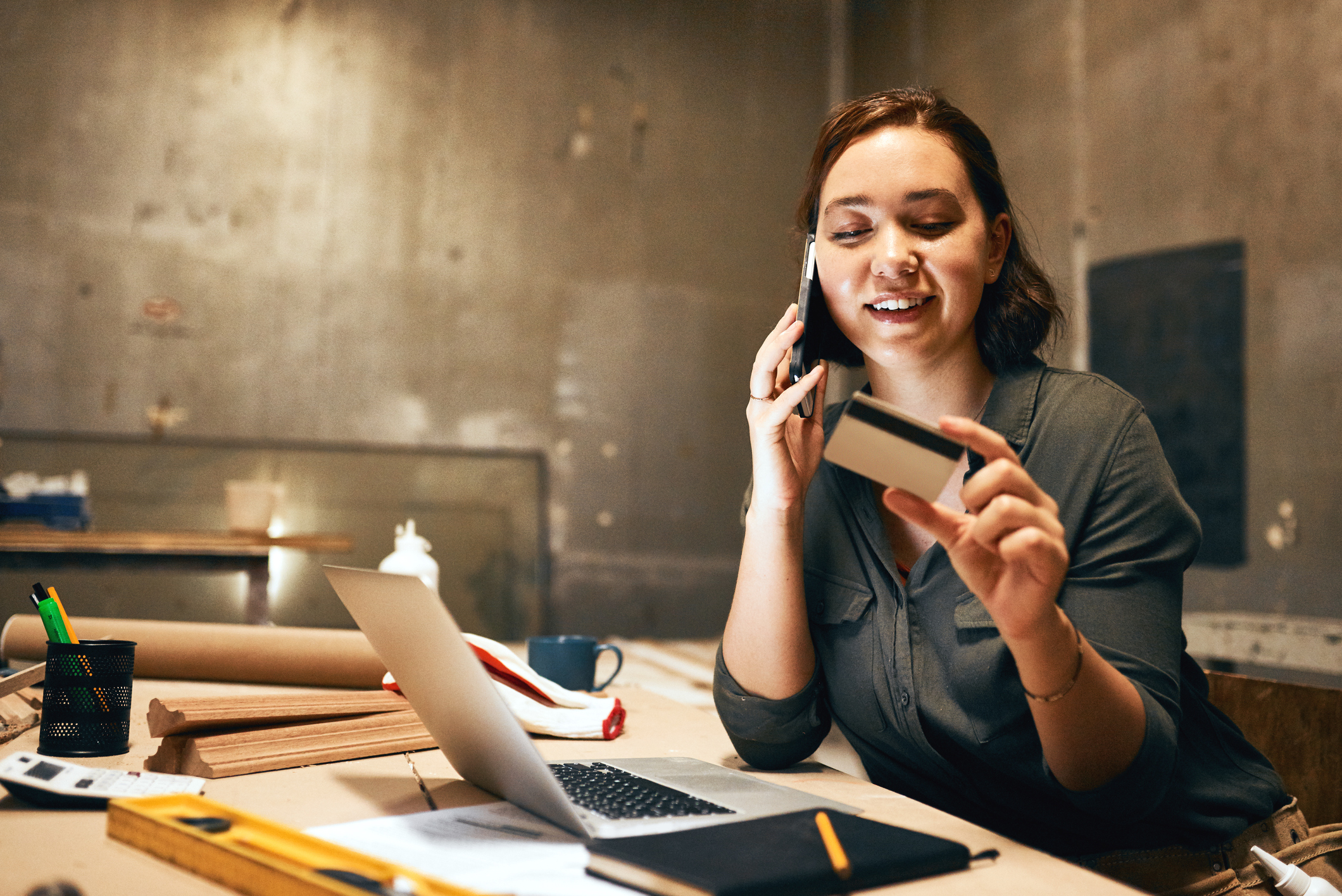 holding her credit card and doing online shopping while talking on her cellphone holding her credit card and doing online shopping while talking on her cellphone