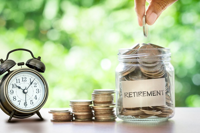A clock sits next to a jar of coins with the word "retirement." A clock sits next to a jar of coins with the word "retirement."