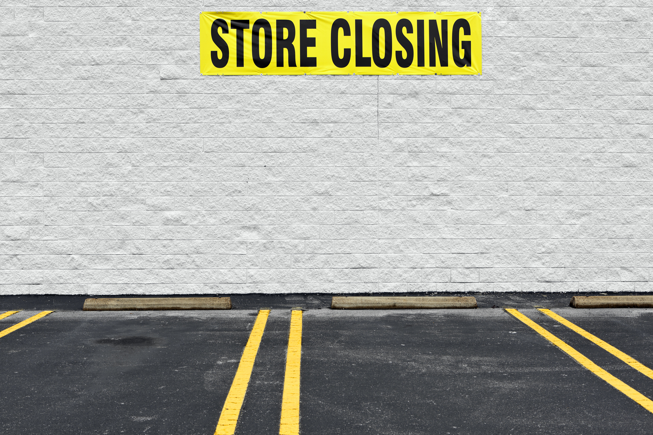 Bright yellow STORE CLOSING sign on a concrete wall.
