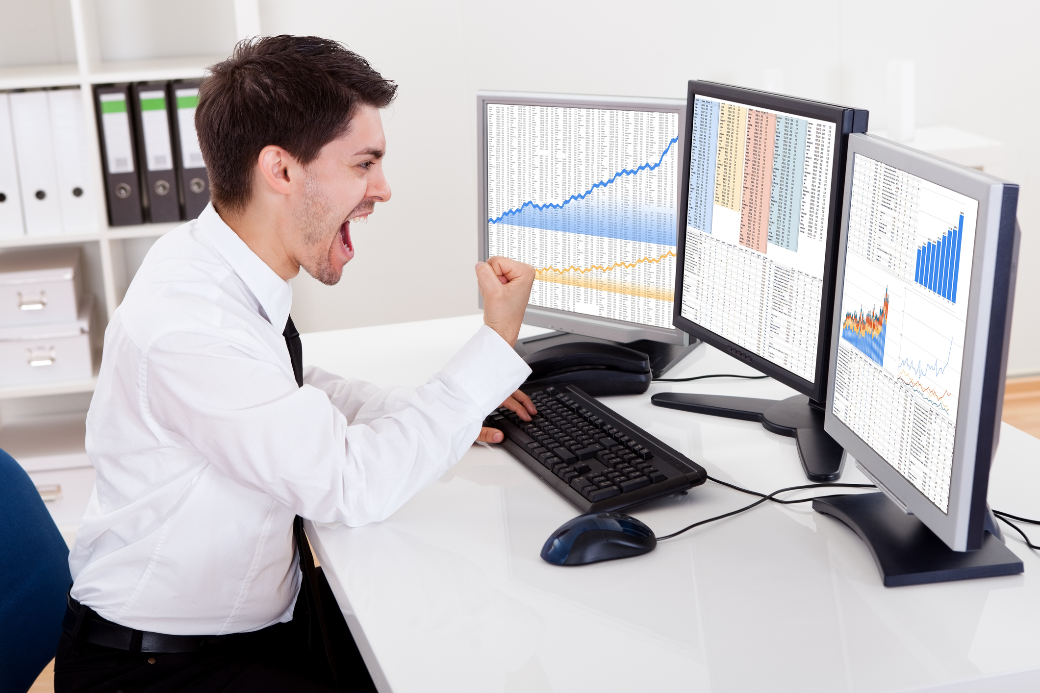 man in office looking at computer screen with stock chart and celebrating -- investing bull market Person in office looking at computer screen with stock chart and celebrating.