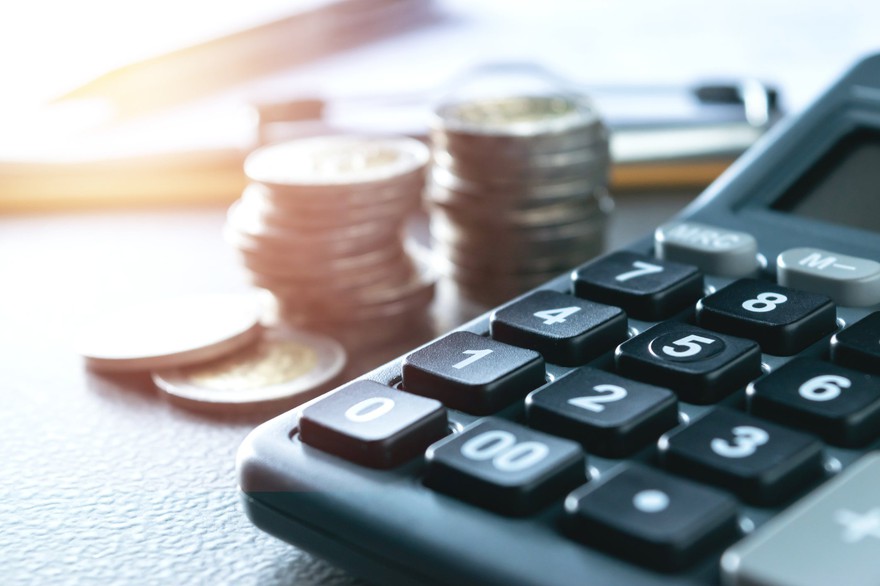 A closeup of a calculator with stacks of coins next to it. A closeup of a calculator with stacks of coins next to it.