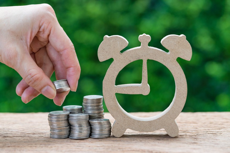 A person stacking coins next to a wood clock cutout. A person stacking coins next to a wood clock cutout.