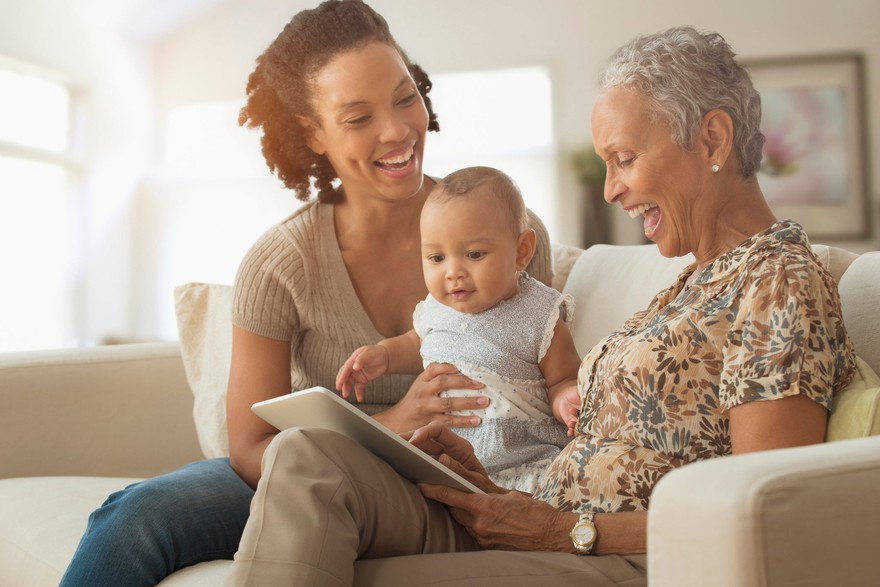 Senior laughs with adult and small child on couch at home. Senior laughs with adult and small child on couch at home.