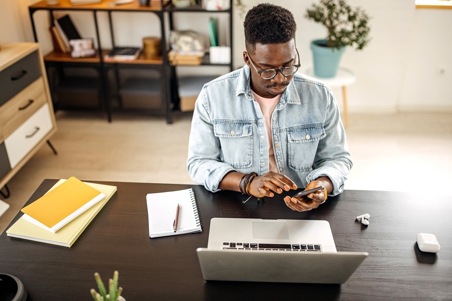 A man sitting at a desk using his phone. A man sitting at a desk using his phone.