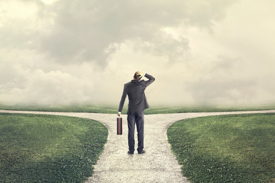 Business man has his hand on his head while looking at a fork in the road. Business man has his hand on his head while looking at a fork in the road.