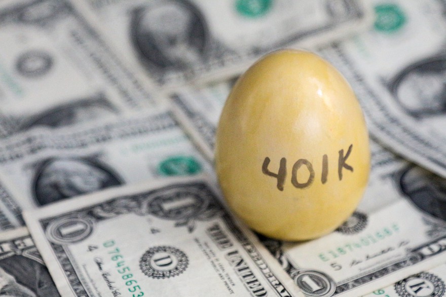 Golden egg with the "401K" written on it stands vertically atop of dollar bills Golden egg with the "401K" written on it stands vertically atop of dollar bills