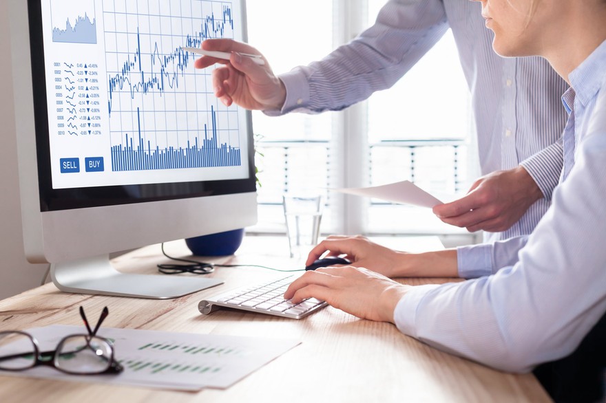 Two professionals looking at stock charts on a monitor. Two professionals researching stock charts on a monitor.