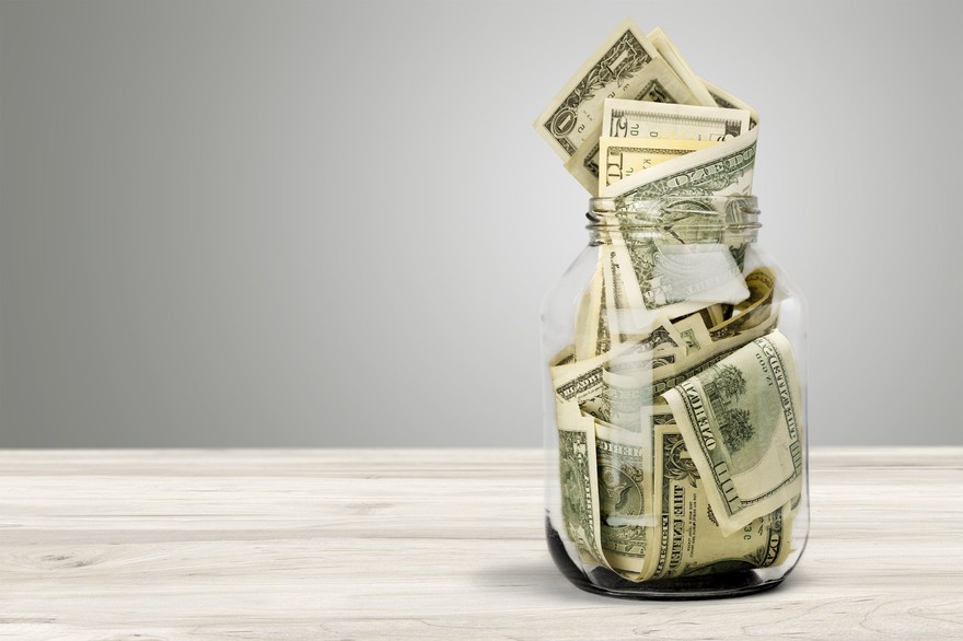 Bills of differing values messily stuffed in a jar sit on a table. Bills of differing values messily stuffed in a jar sit on a table.