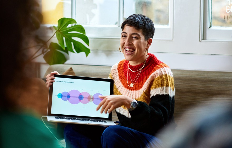 A smiling woman showing the screen on her laptop.