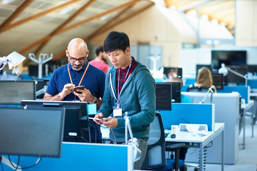 Two men in an office using mobile devices. Two men in an office using mobile devices.