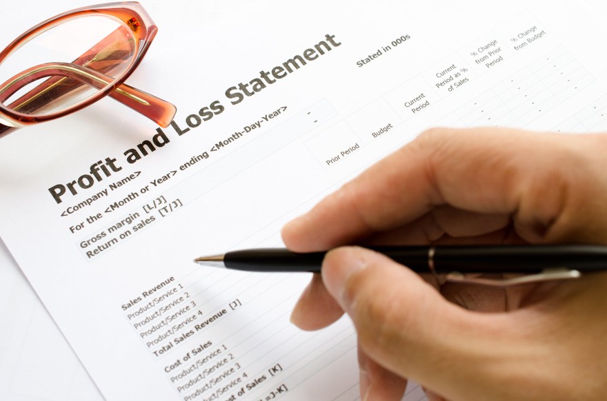 A person marking a profit and loss statement with a pen. A person marking a profit and loss statement with a pen.