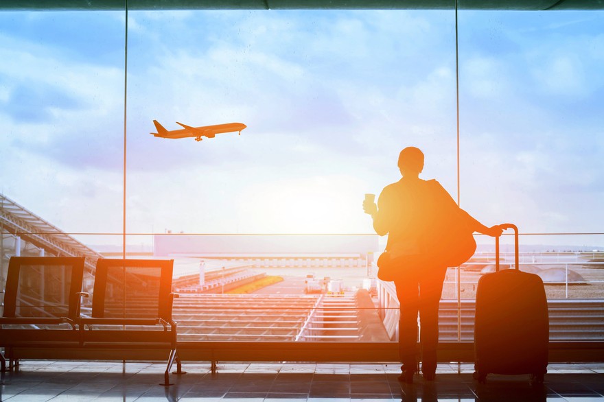 Silhouette of a person in front of an airport window watching a plane take off.