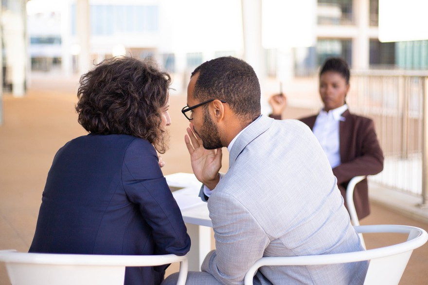 A man and woman talking secretively while another woman watches them. A man and woman talking secretively while another woman watches them.