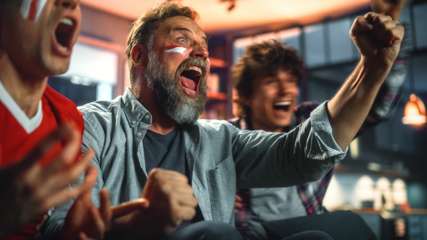 A person placing a sports bet on a smartphone. Sports fans cheering while watching a game.
