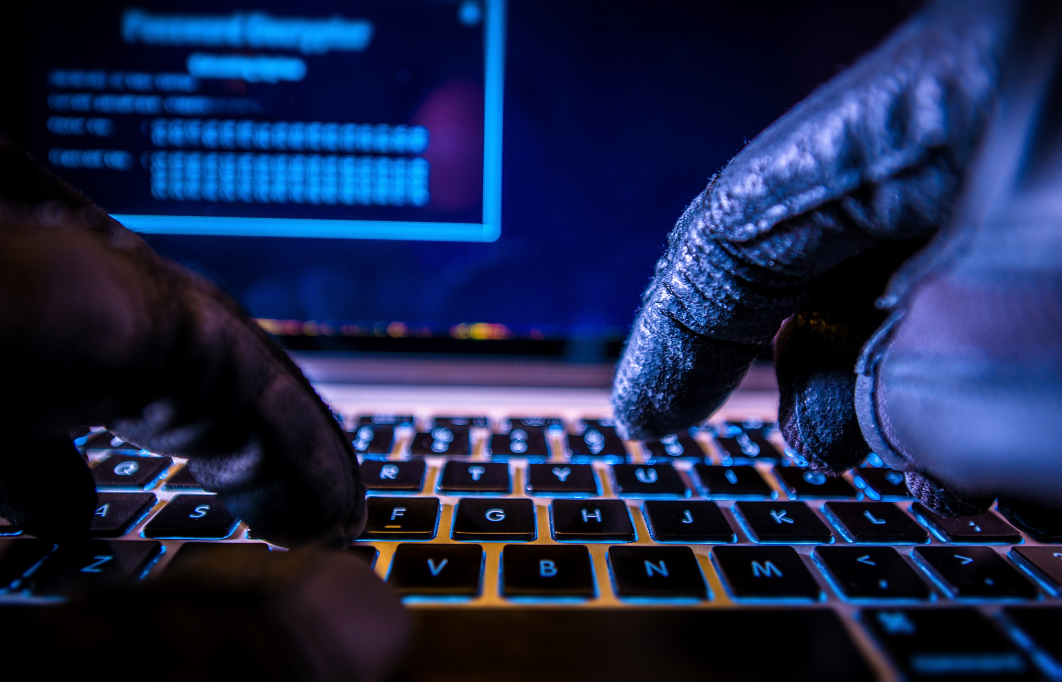 pair of gloved hands typing on laptop keyboard -- hacker cyber attack Hacker with black leather gloves typing on laptop keyboard.