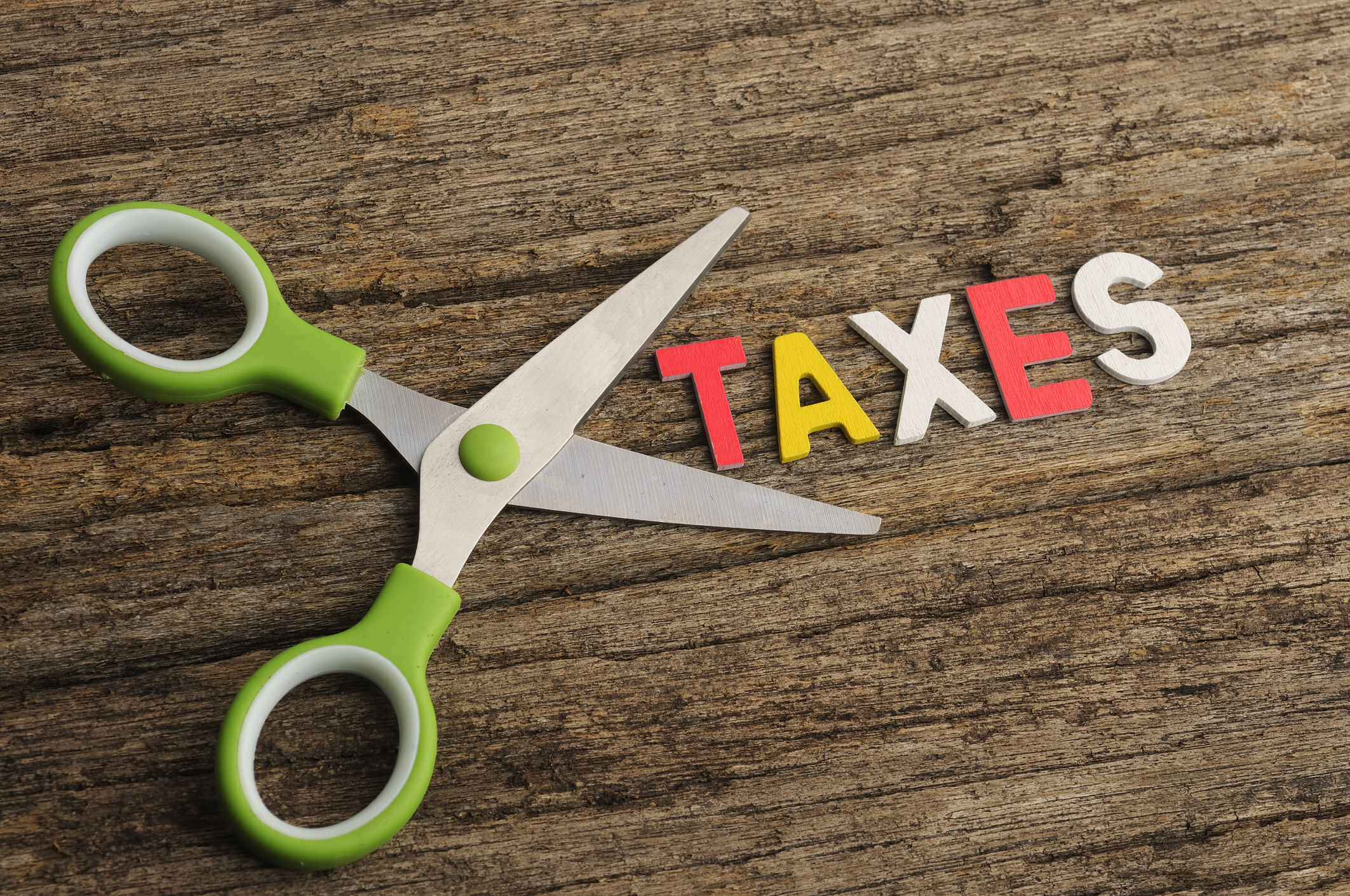 Scissors lying next to word Taxes -- tax cut deduction credit Safety scissors lying next to the word Taxes.