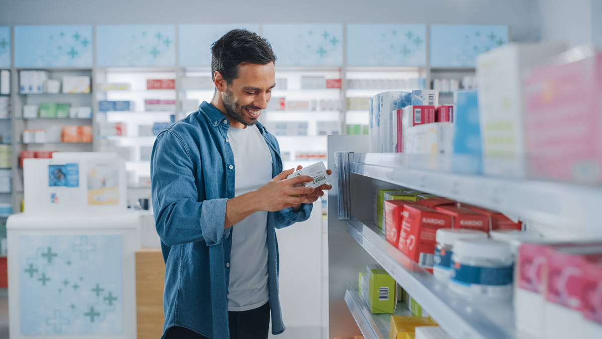 A person smiling while holding a product in a box at a pharmacy.