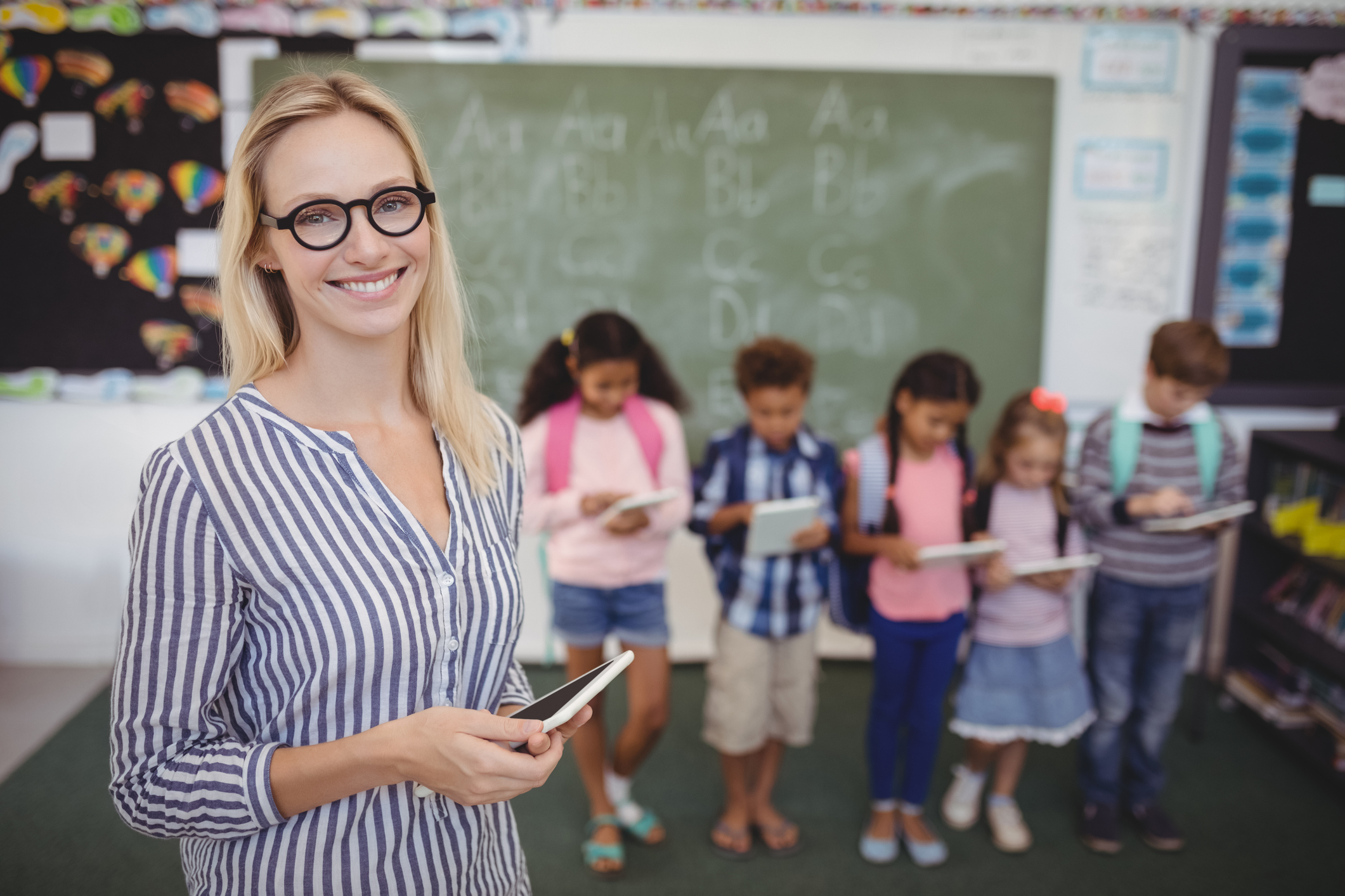 school teacher standing in front of students and holding tablet -- public employee 403b school teacher standing in front of students and holding tablet -- public employee 403b