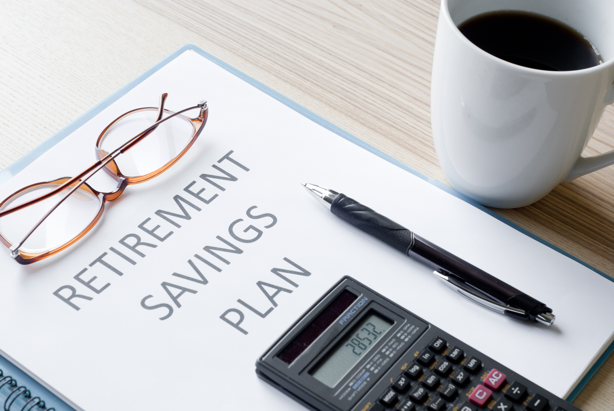 Paper titled Retirement Savings Plan with pen, reading glasses, and coffee nearby.