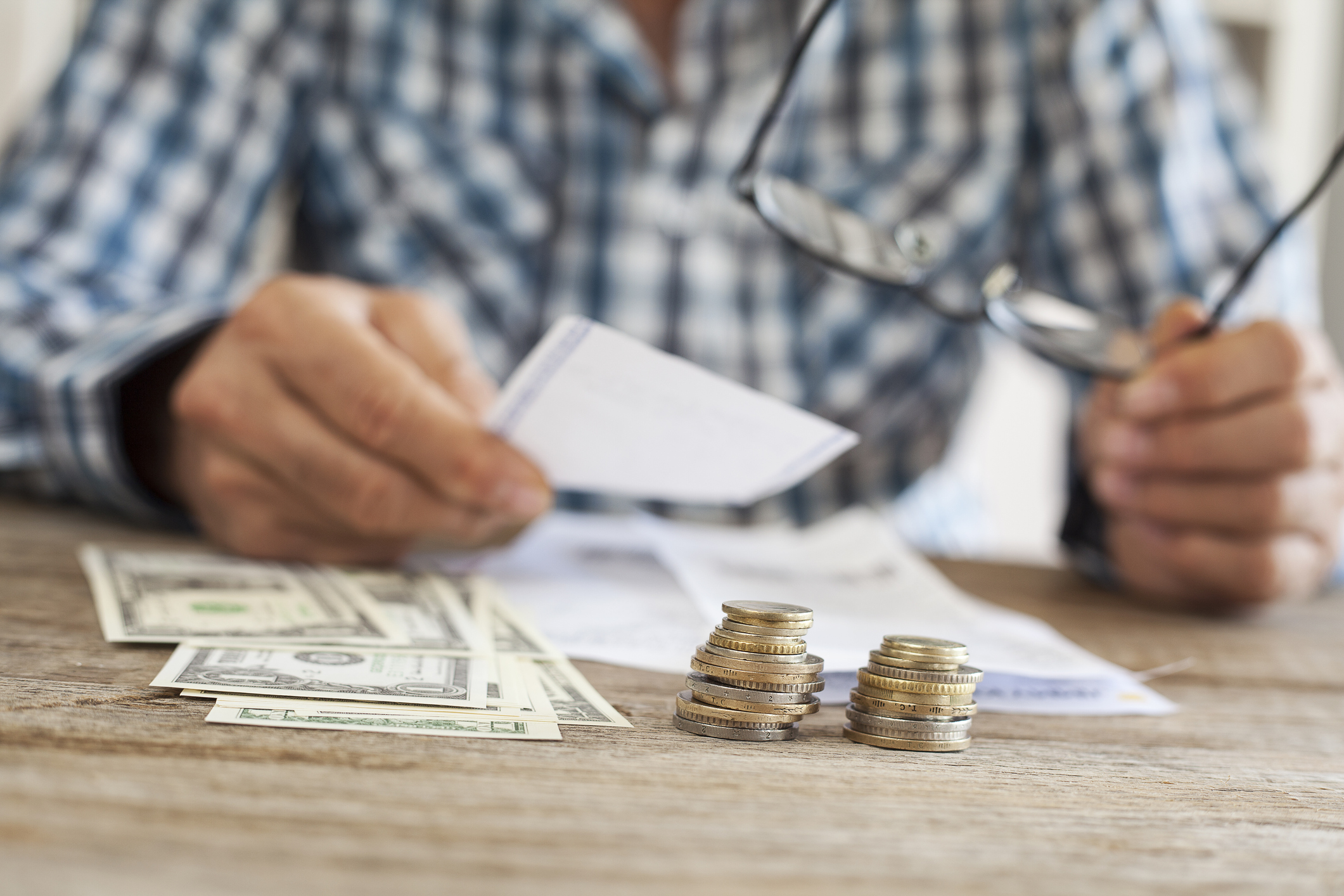 Man sorting paperwork on a table with dollars and coins sitting nearby.