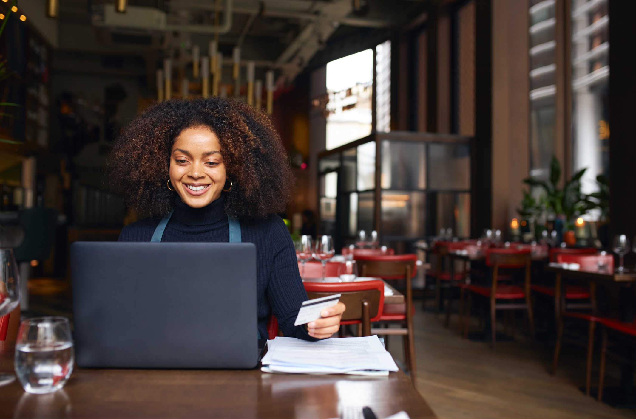 small business owner A person working in a café and holding a credit card while processing a customer's payment at a laptop.