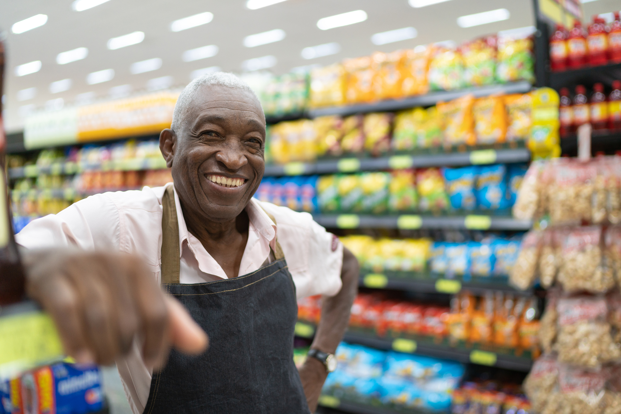 smiling-senior-working.jpeg Person wearing an apron in a supermarket smiles.