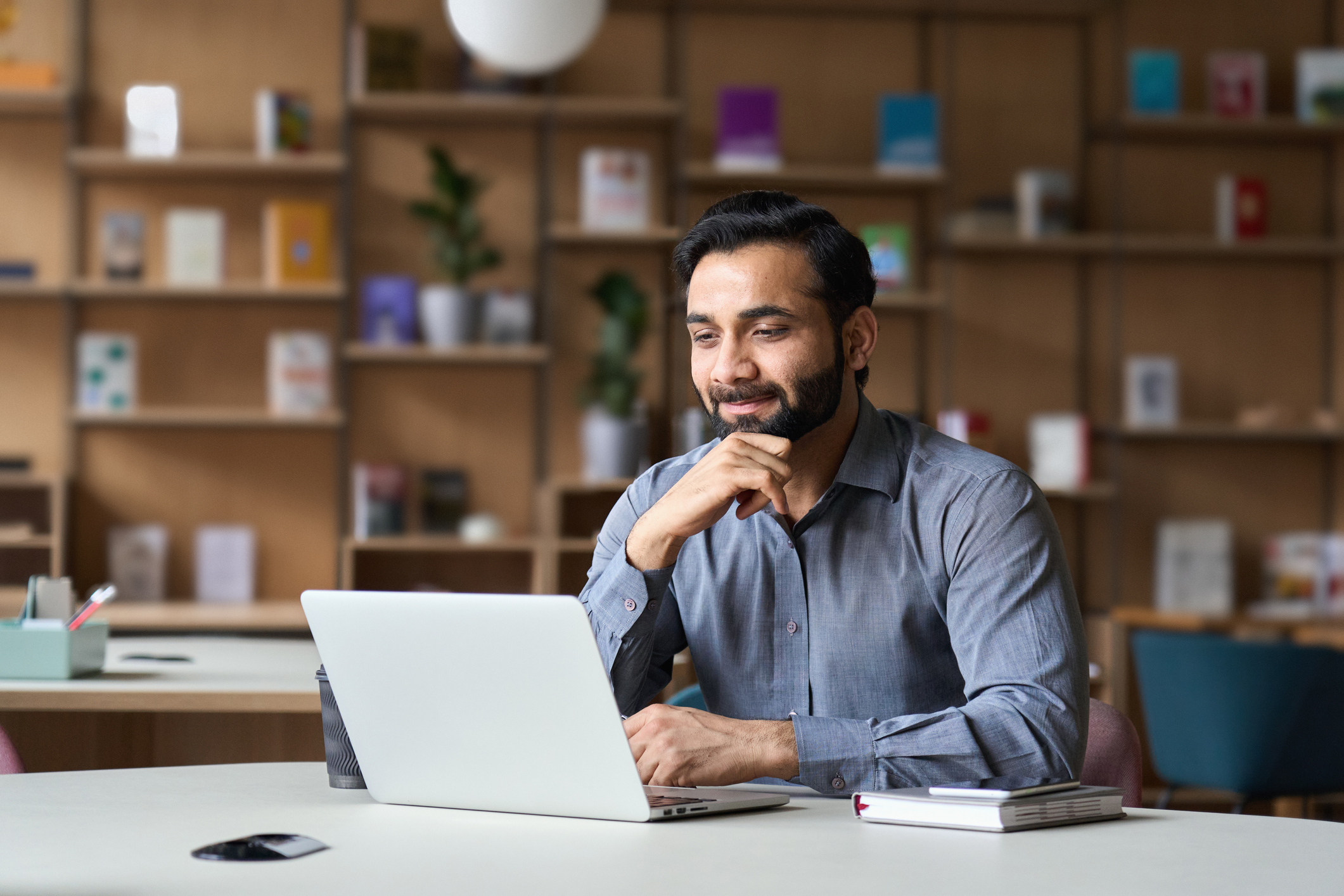 smiling_bearded_businessperson_working_on_laptop Smiling person working on laptop in modern office.
