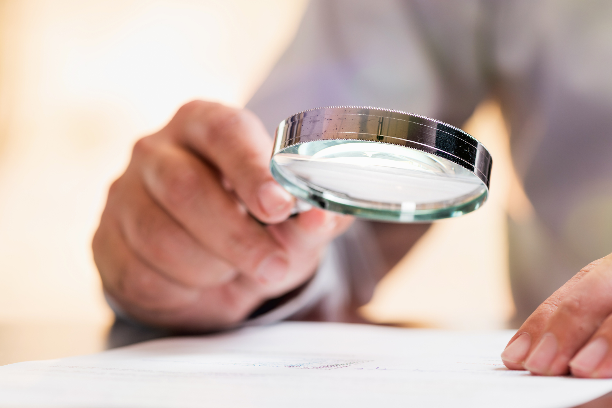 take a close look research fine print examine magnifying glass study A person uses a magnifying glass to thoroughly examine financial documents.