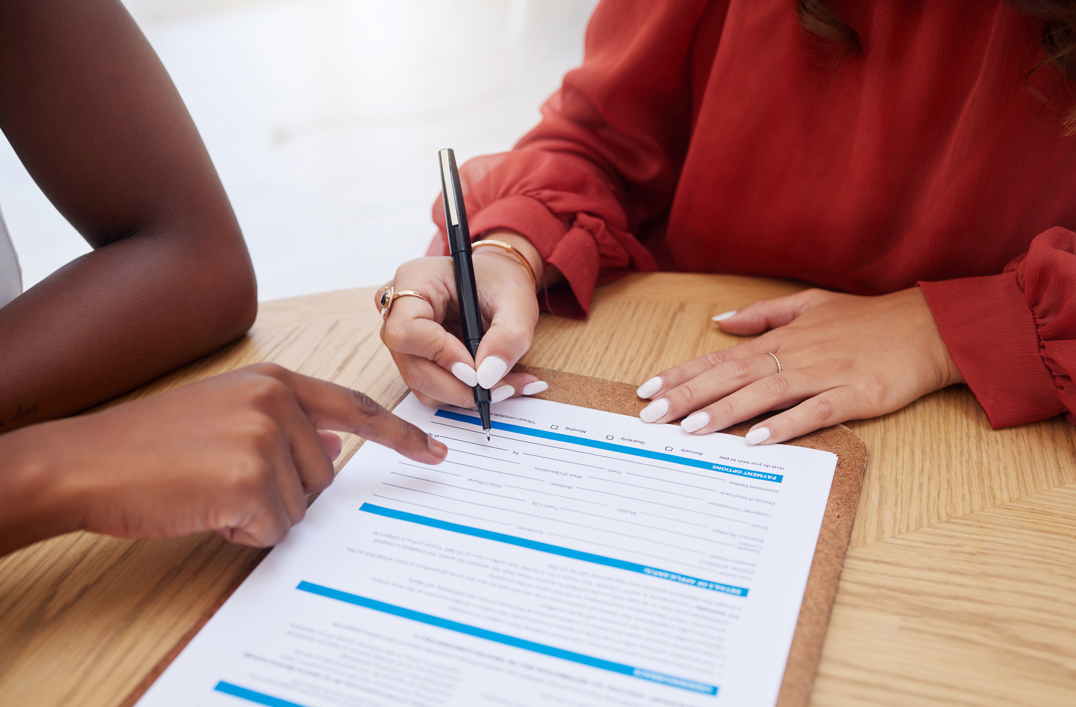 Two people signing documents Close-up shot of a document on a table, with one person pointing to where the other person should sign it.