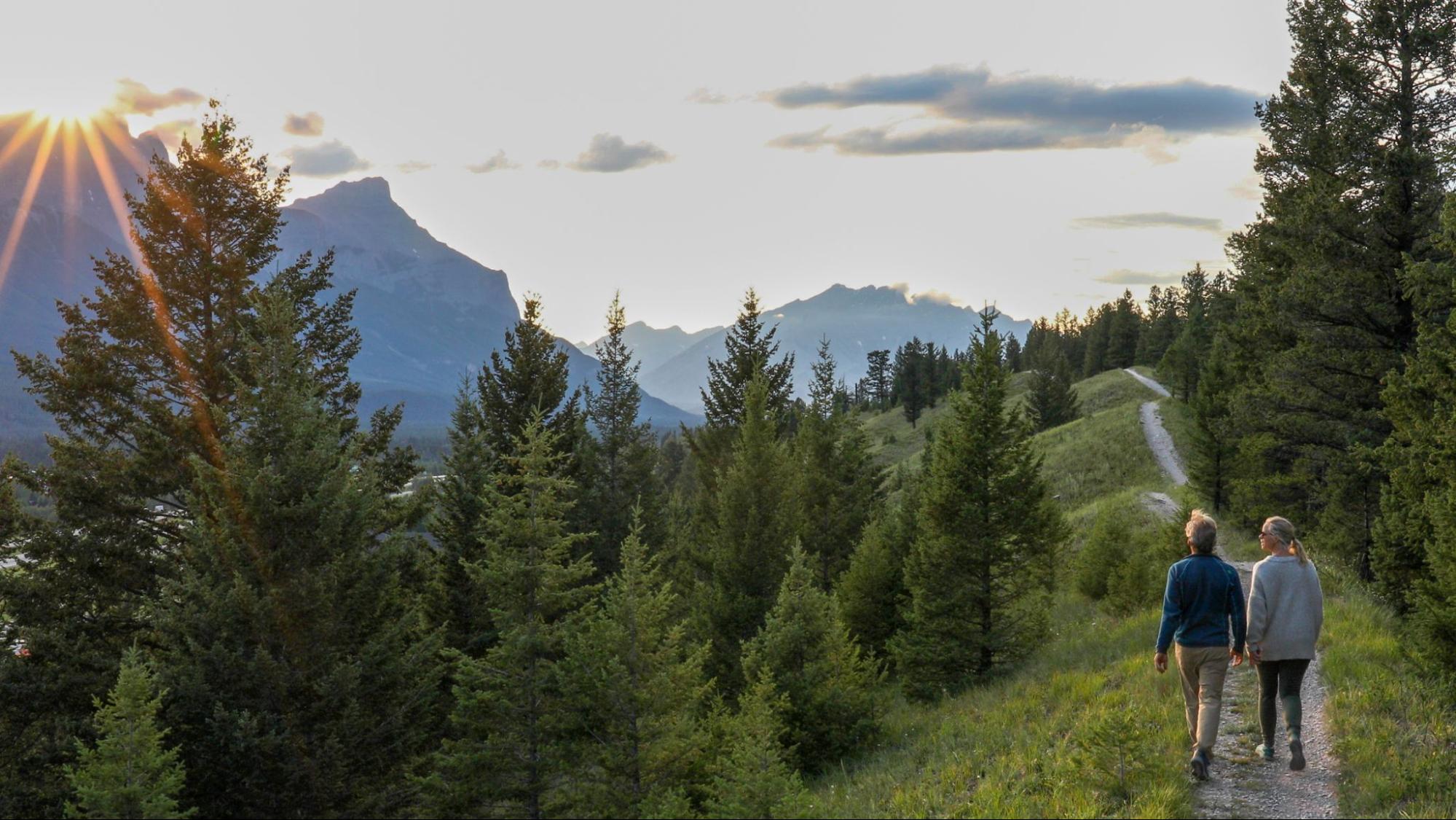 Two people walking in nature. Two people walking along a trail in the mountains as the sun sets over a mountain.