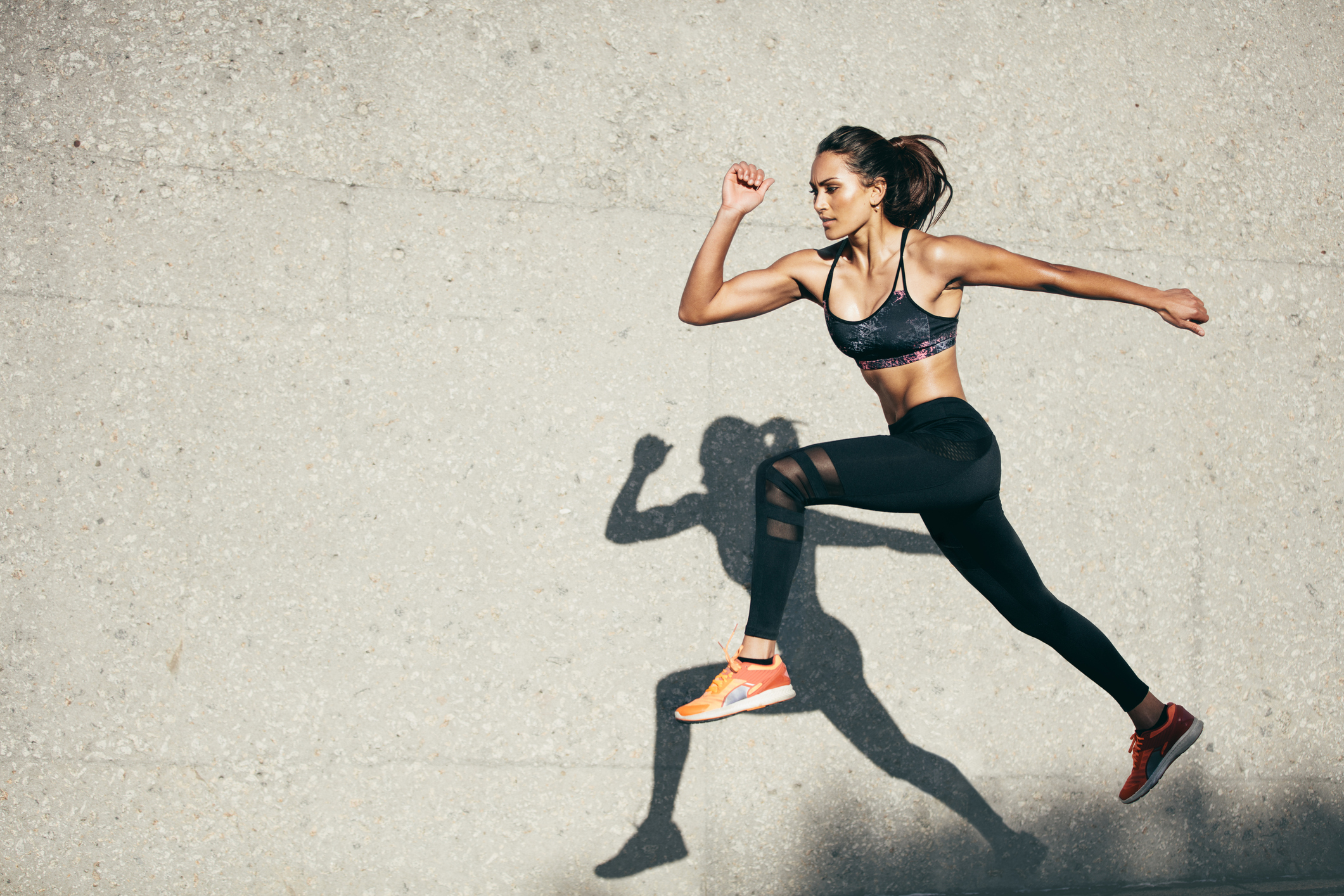 Woman in athletic gear striking a pose. Person in athletic gear racing their shadow on the wall behind them.