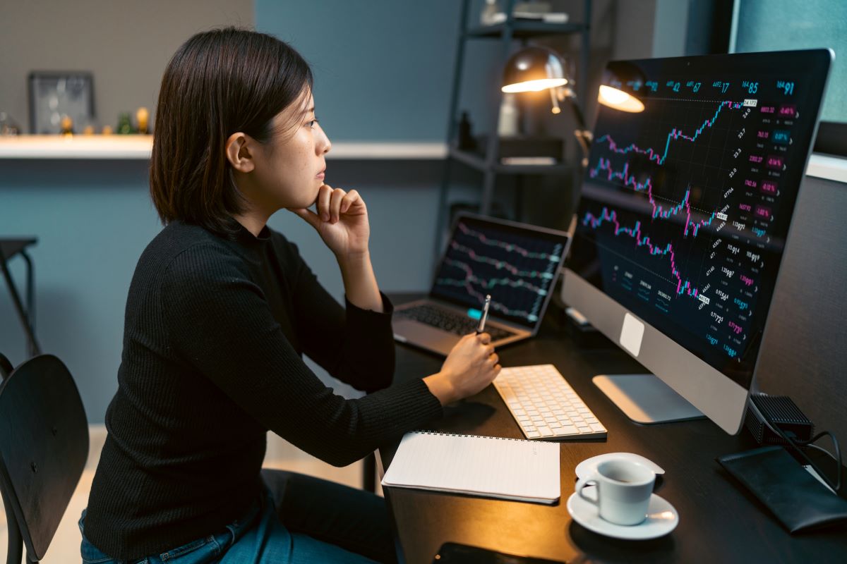 women-investing-stock-graphs A women sitting at a desk reviewing stock charts on a computer.