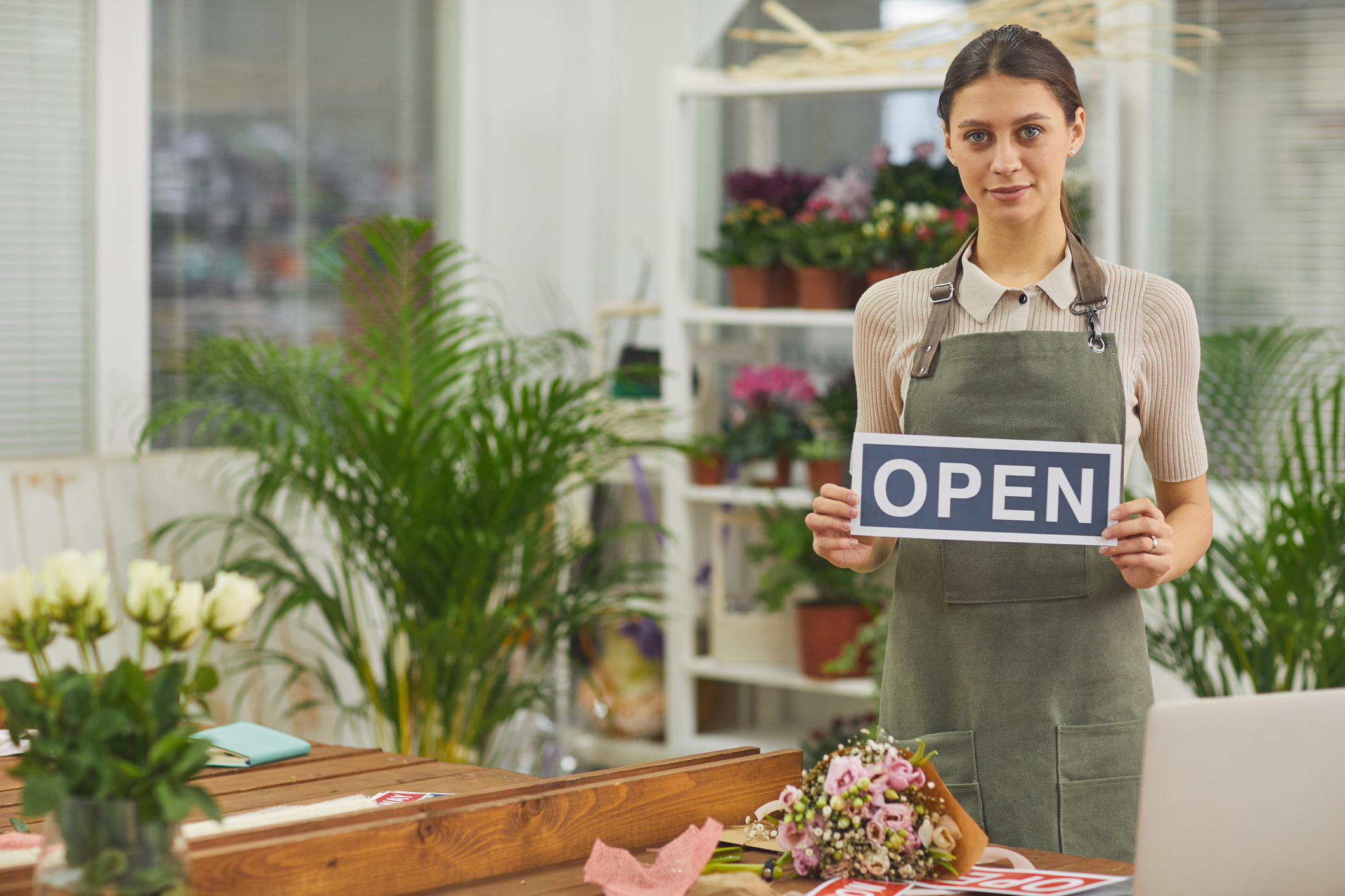 Worker in floral shop holding open sign Worker in floral shop holding open sign.