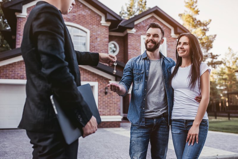 Couple being handed keys in front of brick house