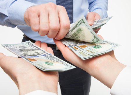 close up of man handing several 100 dollar bills to someone