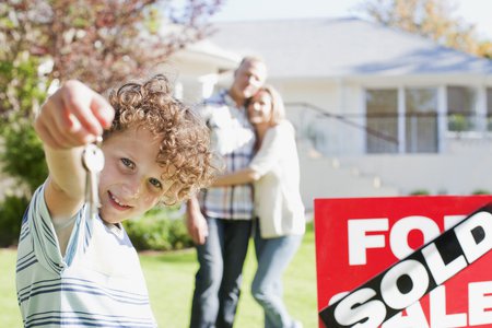 Kid with keys in front of house with sold sign and parents