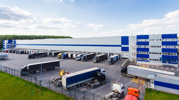 A fleet of tractor-trailers parked in a warehouse parking lot.