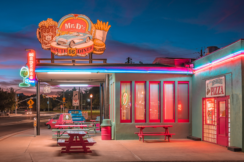 A red and turquoise diner has red picnic tables outside the establishment.